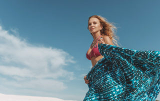 Eine Frau geht im Bikini am den Strand entlang und trägt einen Pareo mit Walhai Musterung.